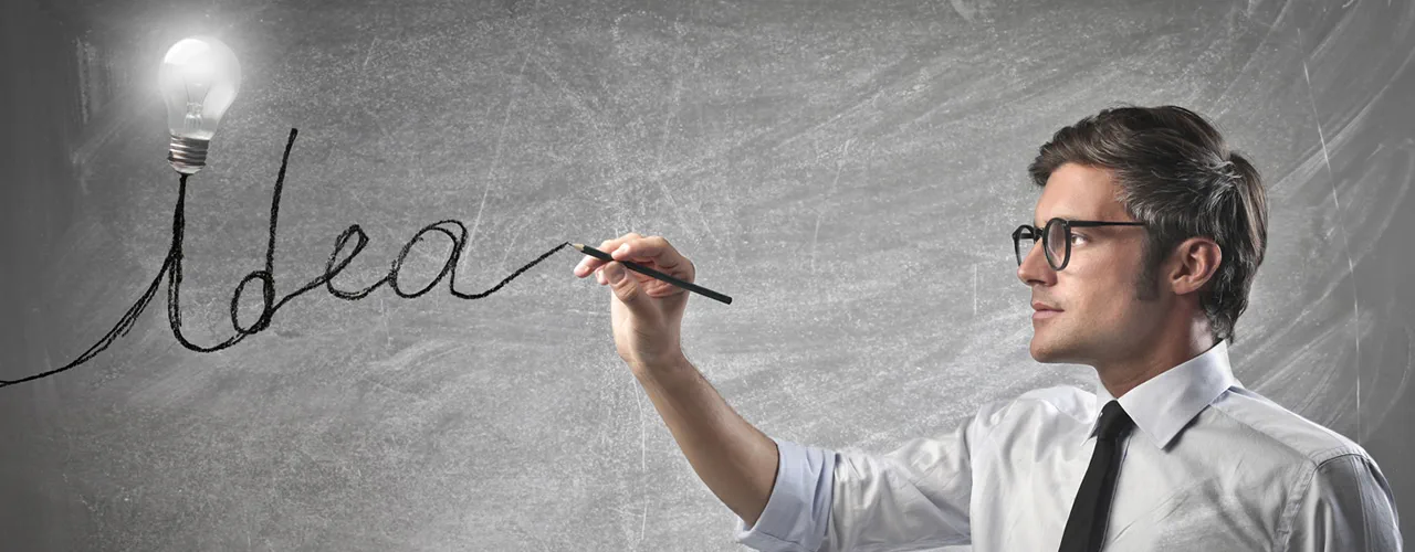 A man drawing the word Idea on a chalkboard, its line leading to a lightbulb